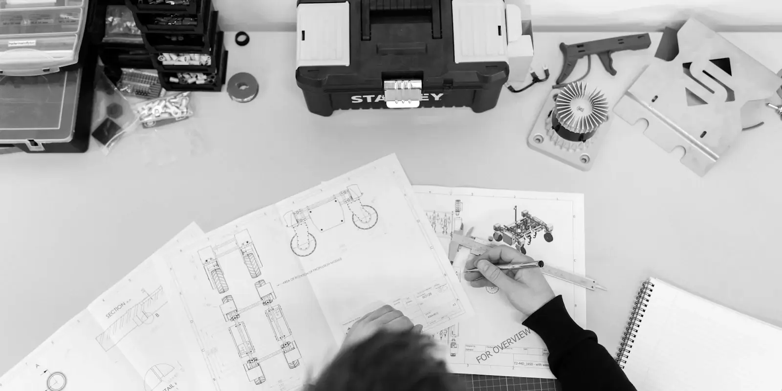 Dibujos técnicos y herramientas en una mesa de trabajo, con alguien trabajando en un diseño.